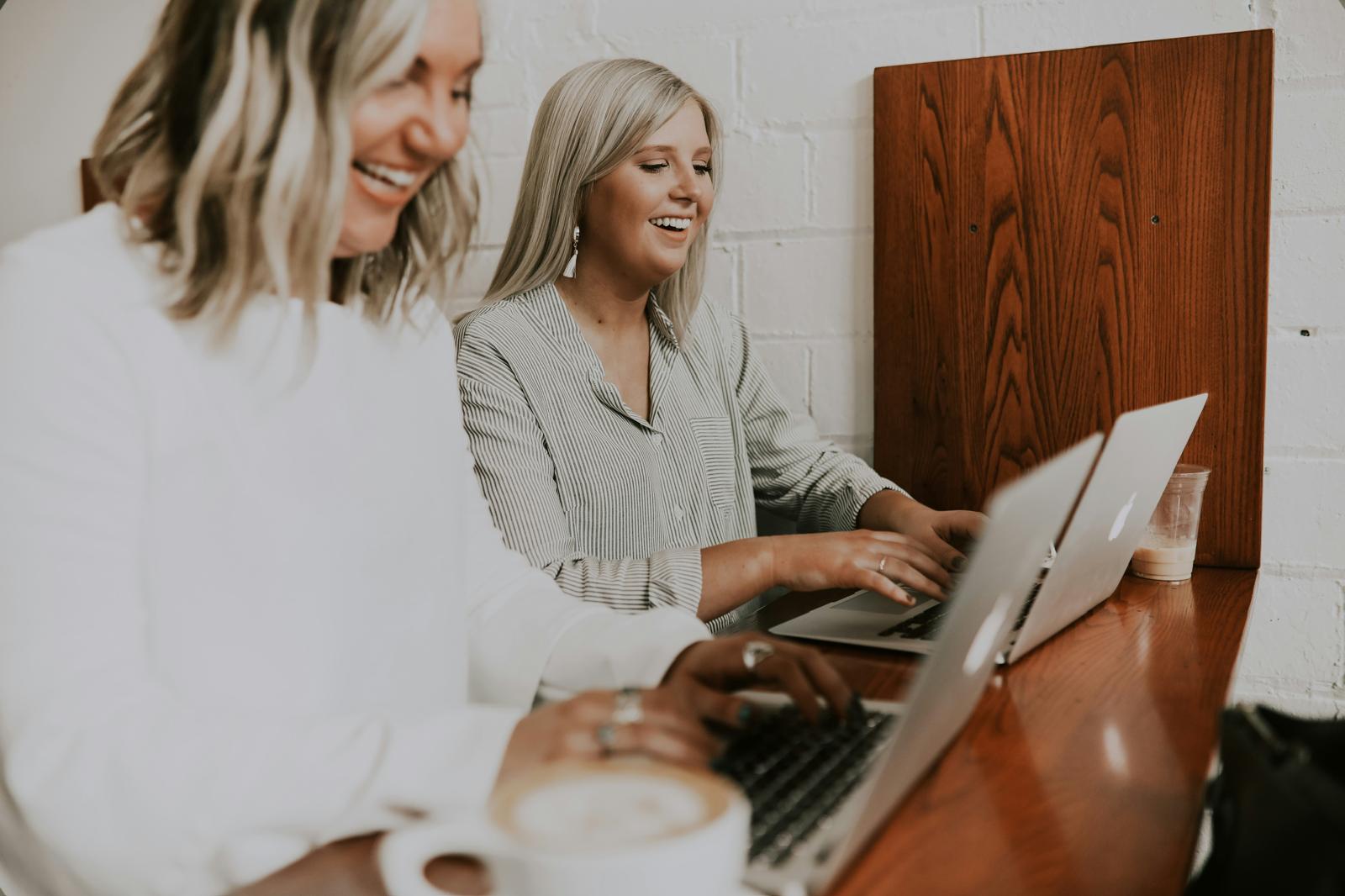 Two women laughing while working on laptops