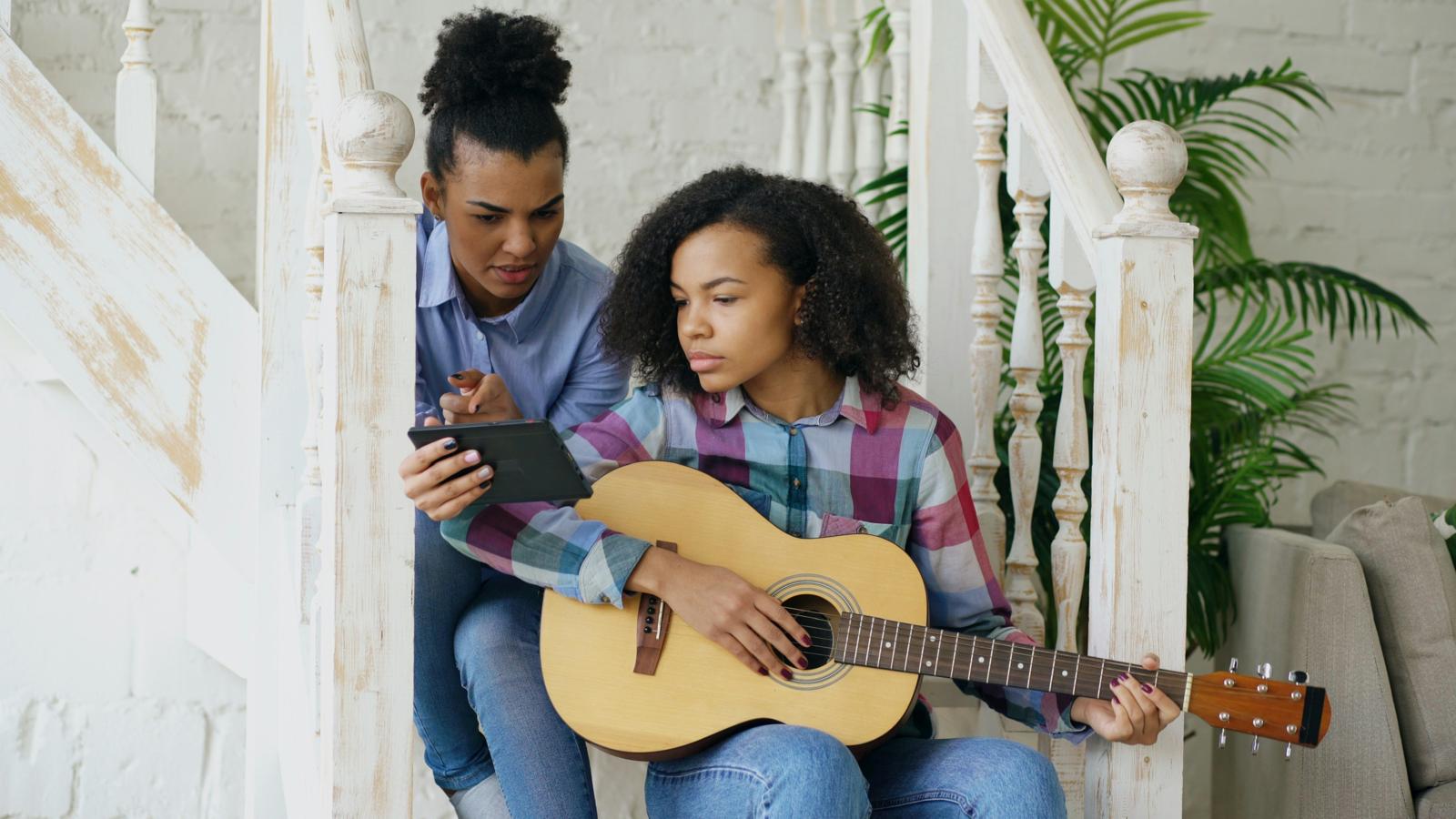 A woman and a teenage girl playing guitar together on a staircase
