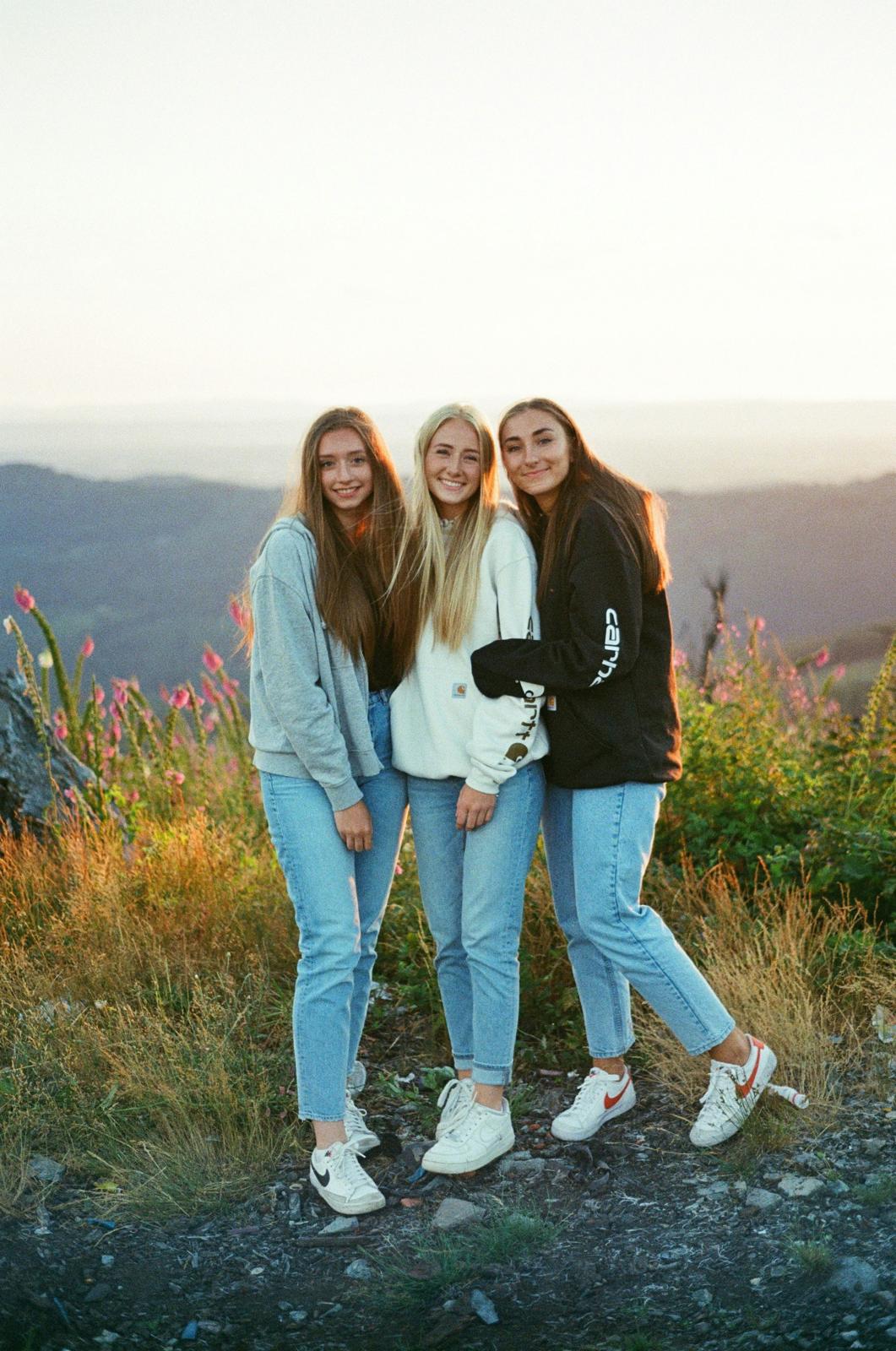Three young women standing together on a hilltop at sunset
